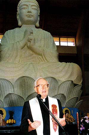 A Catholic priest speaking before a large Buddhist statue