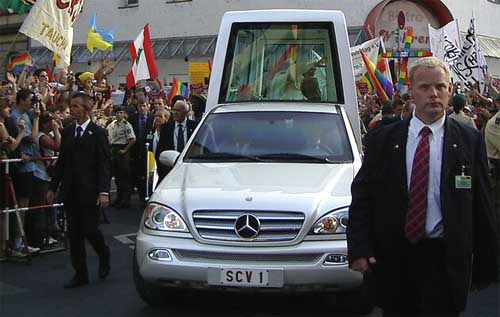 Benedict in the Popemobile with rainbow flags waving in the crowd