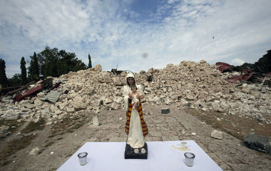 A statue of Our Lady and the Child Jesus standing amidst ruines