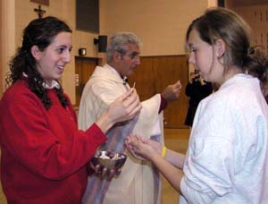 A priest and female Eucharistic minister giving communion in the hand