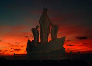 A statue of a boat with Our Lady during a sunset