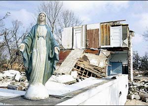 A Statue of Our Lady stands amidst wreckage from a flood